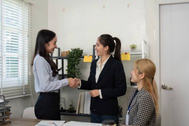 Pozitif bir toplantıda iki kadın el sıkışırken, diğeri izliyor, takım çalışmasını ve mali planlamada başarıyı kutluyor..