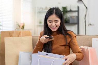 Neşeli bir kadın internetten alışveriş yaparken etrafındaki renkli torbalarla alışveriş deneyiminin tadını çıkarıyor..