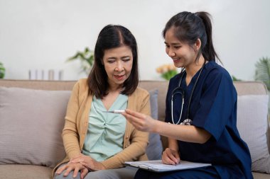 Bakıcı, yaşlı bir hastaya semptomları ve tedavi seçeneklerini tartışan bir termometre gösterir..