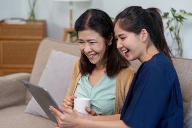 Bakıcı ve hasta, bir tablete bakıp bakıcılığın önemini vurgulayan bir kahkahayı paylaşırlar..