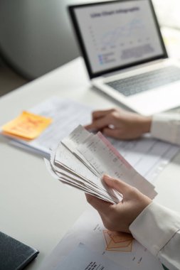 Bir kişi akıllı telefondaki mali bilgileri incelerken vergi belgelerini yönetir, maliyedeki birden fazla görevi vurgular.