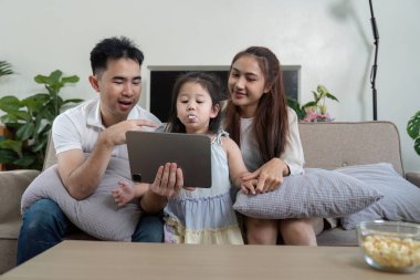 Bir aile bir tabletle meşgul olur, birlikte eğlenceli bir anı paylaşır, günlük hayatlarındaki sevgi ve bağlantıyı resmeder..