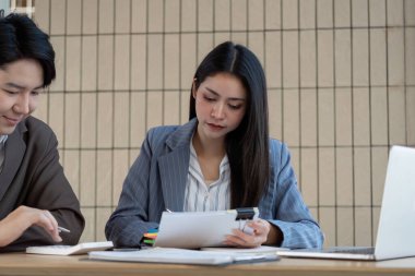 Bir muhasebeci, takım arkadaşı takım çalışması ve analiziyle ilgili bir tartışmaya girerken mali evrakları inceler..