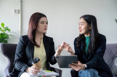 İki profesyonel kadın, bir tablet ve kahve kullanarak, takım çalışması ve stratejik planlamayı vurgulayarak bir tartışmaya giriştiler..