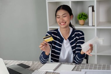 Bir kadın dizüstü bilgisayarını kullanıyor ve kredi kartını elinde tutarken mali ve evrak işlerini yürütüyor..