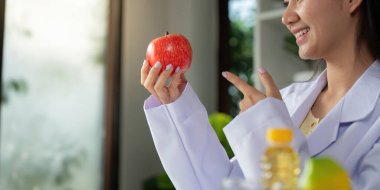 Bir beslenme uzmanı canlı bir elma sergiliyor, sağlıklı beslenme alışkanlıklarını destekleyen bir gülümsemeyle sağlık yararlarını tartışıyor..