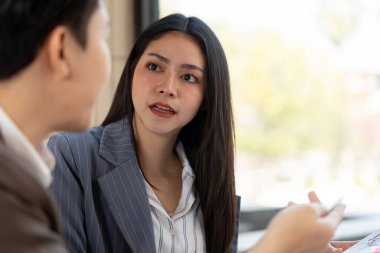 Bir kadın, erkek meslektaşı ile dikkatlice tartışıyor, profesyonel işbirliği ve parlak ofis ortamındaki ortak hedeflerini vurguluyor..