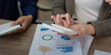 Odaklanmış bir profesyonel, mali verileri ve ortak ofis ortamındaki raporları incelerken hesap makinesi kullanır.