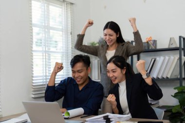 Çeşitli bir ekip parlak bir ofiste başarılarını sevinçle kutluyor, takım çalışmalarını ve heyecanı ön plana çıkarıyorlar..