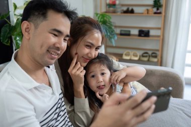 Neşeli bir aile, kanepede akıllı telefon kullanırken neşeli etkileşimler kurar, gülümsemelerini paylaşır..