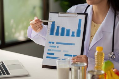 Bir beslenme uzmanı beslenme istatistiklerini açıklamak için bir çizelge kullanır, bir müşteri toplantısında beslenme ve sağlık analizlerindeki uzmanlığını gösterir.