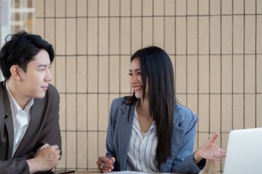 Profesyonel kıyafetli bir erkek ve bir kadın, bir toplantıda proje planlarını tartışıyorlar. Kadın hareketli bir şekilde düşüncelerini paylaşıyor, takım çalışmasını ve girişimini yansıtıyor..