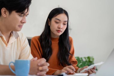 Bir çift, hesap makinesi ve belgeleri kullanarak mali durumlarını tartışmaya odaklanıyor. Etkileşimleri mali planlamada takım çalışmasının önemini gösteriyor..