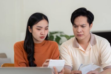 Bir çift, faturalara bakarak ve bütçelerini değerlendirmek için bir hesap makinesi kullanarak finansal planlamalarına derinden odaklanmış durumda. İfadeleri endişe ve ciddiyet taşıyor..