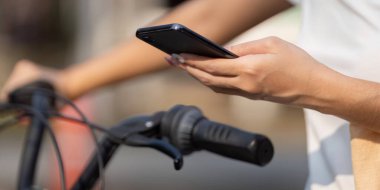 Bir insan bisikletinin gidonunu tutarken akıllı telefonunu kontrol eder. Çevre dostu seyahatin kolaylığını vurgular..