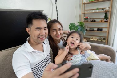 Neşeli bir aile kanepede birlikte eğlenceli bir anı yakalar, gülümser ve akıllı bir telefonla poz verir..