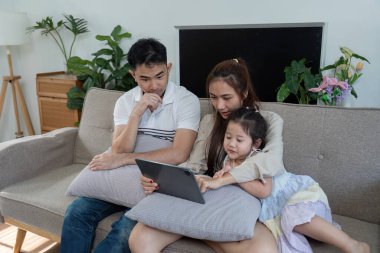 Üç kişilik bir aile kanepede tabletle meşgul, gülümsemelerini ve iletişim anlarını paylaşıyorlar..