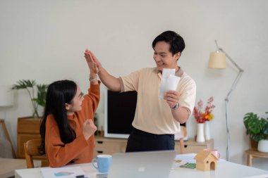 Genç bir çift, mali başarılarını sıcak bir yuva ortamında kutlarken neşe ve takım çalışması sergiliyor..