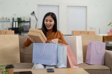 Neşeli genç bir kadın, yeni eşyaları için heyecanla online alışverişini yapıyor..