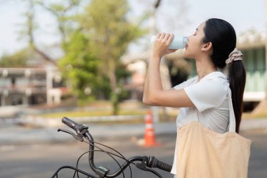 Genç bir kadın bisikletinin yanında dikilirken bir yudum alır, sürdürülebilir ve aktif bir yaşam tarzını somutlaştırır..