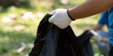 Eldiven giyen bir kişi parkta çöp topluyor, temiz bir çevreye ve sürdürülebilirlik çabalarına katkıda bulunuyor.