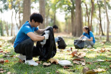 Canlı bir parkın ortasında, bir gönüllü çevresel bilinci göstererek, bir topluluğun temizliğinin etkisini artırmak için çöp ayıklamaya odaklanır..