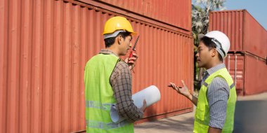 İki mühendis lojistik planlamasında işbirliği yapıyor, planları gözden geçiriyor ve konteynır deposunda proje detaylarını tartışıyorlar..