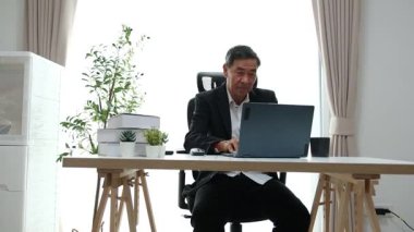 Asyalı büyükbaba bilgisayarındaki bilgileri güncellerken oturup günlük haberleri izliyor ve güncel olaylardan haberdar oluyor..