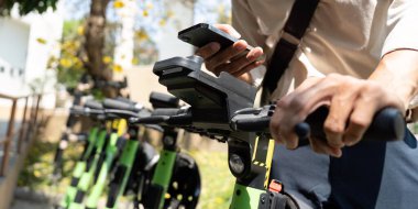 Bir şehir bisikletçisi binmeye hazırlanırken akıllı telefonuyla etkileşime geçiyor, bu da şehirlerdeki teknoloji ve çevre dostu ulaşımın karışımını simgeliyor..