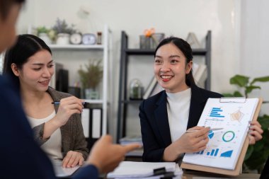 Parlak bir ofis alanında, neşeli bir kadın takım arkadaşlarına grafikleri ve trendleri açıklar ve bilgili kararlar almada verilerin önemini gösterir..