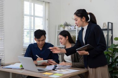 Modern bir çalışma alanında, üç profesyonel stratejik bir tartışmaya girer, notları gözden geçirir ve daha iyi sonuçlar için fikir üretir..