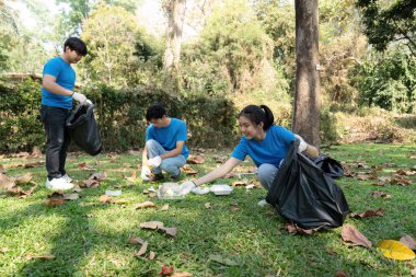 Bir grup gönüllü birlikte çalışır, çöp toplar ve çimenli bir park alanından çöp toplar, sürdürülebilirlik çabalarındaki takım çalışmalarını vurgularlar.