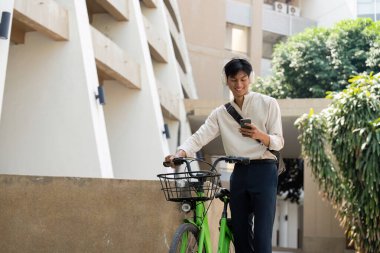 Şehir manzarasının ortasında, bu genç adam akıllı telefonunu, çevre dostu bisikletiyle eşleştirerek, modern sürdürülebilir ulaşımı resmediyor..