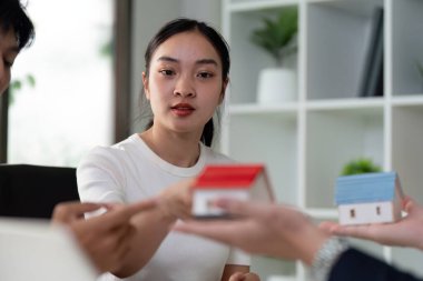 Bir çift modern bir ofiste emlakçıyla iletişim kuruyor. Mini ev modellerini ev satın alma seçeneklerini düşünürken görüyorlar..