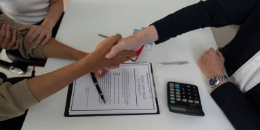 Pazarlıklardan sonra bir çift, emlakçılarının rehberliği ile alışverişlerini onaylayan bir tokalaşmayla anlaşmayı imzalıyor. Bu an güven ve bağlılığı simgeliyor..