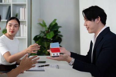 Profesyonel bir ortamda, bir emlakçı yeni evleri için uygun seçenekleri vurgulayarak bir çifte minyatür evler sunar..