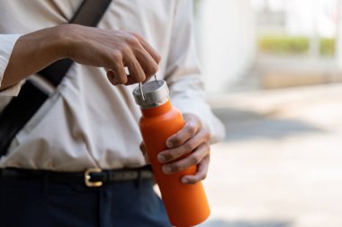 Bir adam turuncu yeniden kullanılabilir su şişesini açarken görülüyor, sürdürülebilir hidrasyon seçeneklerini sergiliyor ve plastik atığı en aza indiriyor..