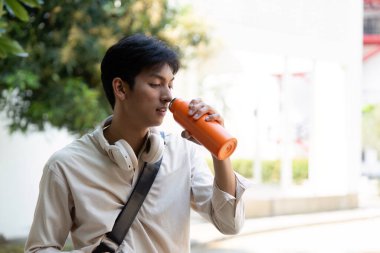 Bu genç adam, canlı turuncu su şişesinden açık hava ortamında su içerken çevre dostu yaşam tarzıyla eğleniyor..