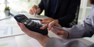 Modern bir ofiste, meslektaşlar mali belgeleri ve hesaplamaları inceleyerek, bilgilendirilmiş karar verme mekanizması verilerinin analiz edilmesinde takım çalışmasını vurguluyorlar..