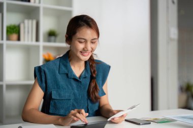 Neşeli bir kadın, bütçe düzenlemesinin önemini gösteren tablet ve kayıt materyalleriyle finansal durumunu etkin bir şekilde yönetiyor..