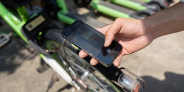 Bisiklet kilidinin üzerinde duran bir el, akıllı telefonların sürdürülebilir ulaşım için ortak bisikletlere erişimin kolaylaştırılmasındaki rolünü vurguluyor.