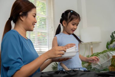 Anne-kız olarak yakalanan neşeli bir an geri dönüşüm için eşyaları ayırırken, sürdürülebilir alışkanlıkları güçlendirirken aynı zamanda çevresel uygulamalar üzerinde bağ kuruyor..