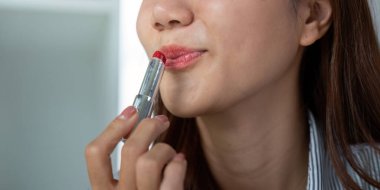 Sakin bir ortamda, bir kadın dudaklarını canlı bir rujla büyütüyor, benzersiz tarzını ve detaylara olan ilgisini ifade ediyor..