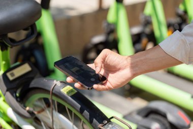 Bir birey bisiklet paylaşım programında yeşil bir bisikleti açmaya hazır bir akıllı telefonu elinde tutuyor, kentsel dönüşüm için sürdürülebilirlik çözümlerini kucaklıyor.