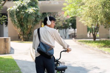 Bir bisikletçi, yemyeşil bir alanda bisiklet sürerken kulaklıkla müzik dinler ve kentsel keşiflerde spor ve keyif karışımını örnek verir..