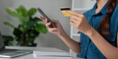 Bir kadın, elinde kredi kartı tutarken finansal bilgilerini kontrol eder. Finansal yönetim ve tasarruflara modern yaklaşımı gözler önüne serer..