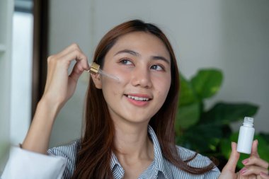 Kadın bir damlacığı tutuyor ve serumu yanağına sürerken gülümsüyor, cilt bakımına ve güzelliğe olan bağlılığını vurguluyor. Bu görüntü özgüveni ve özgüveni temsil eder..