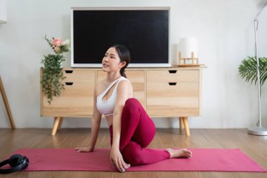 Tutkulu bir yogi kıvrımlı bir duruş takınır, esneklik ve kuvvete odaklanarak antrenman sırasında evinin dinginliğinin tadını çıkarır..