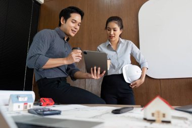 Mühendisler, modern işyerlerinde teknoloji ve işbirliğinin kaynaşmasını gösteren bir tablet üzerinde fikir ve proje ayrıntılarını tartışıyor..