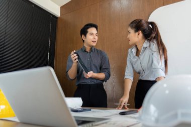 İki mühendis beyin fırtınası yaparak fikir alışverişinde bulunuyor ve plan ve modellerle dolu bir konferans masasının etrafında proje unsurlarını tartışıyorlar..